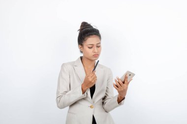 Kurumsal ofis hanımı, siyah saçlı, kalemle oynaşan, resmi olarak akıllı telefonlu beyaz ceketli beyaz arka planlı bir kadın..