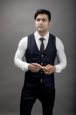 Gri arka planda resmi giyinmiş neşeli, genç ve yakışıklı Hintli iş adamının stüdyo çekimi. Erkek model. Moda Portresi.