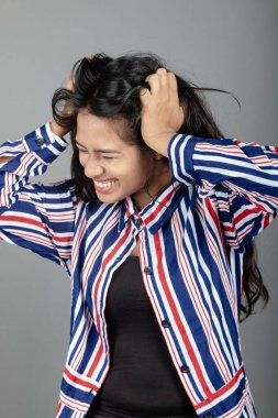 Siyah üst ve kırmızı, mavi, beyaz çizgili tunik giyen, gri arka planda soyutlanmış genç bir Hintli kadının portresi. Genç bayan model, mutlu ve şaşırmış bir ifadeyle saçlarını tutuyor.