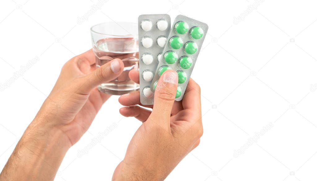 Male hands hold plates of white and green pills and a glass of water on a white background. Copy space. Side view.