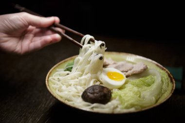  İnsan eli Japon yemek çubuğu ve bir tabak Asya yemeği tutar.