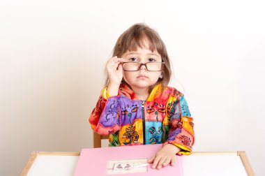 masada oturan ve üzerinde gözlüklerini arıyor küçük kız