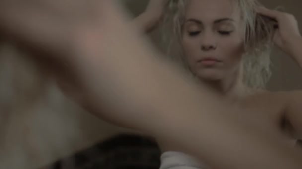 Jeune belle fille blonde se tient devant le miroir et redresse les cheveux . — Video