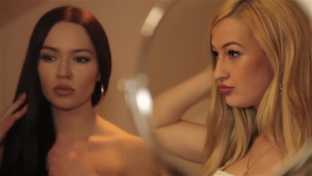 Deux filles blondes et brunes se regardent dans le miroir et corrigent les cheveux . — Video