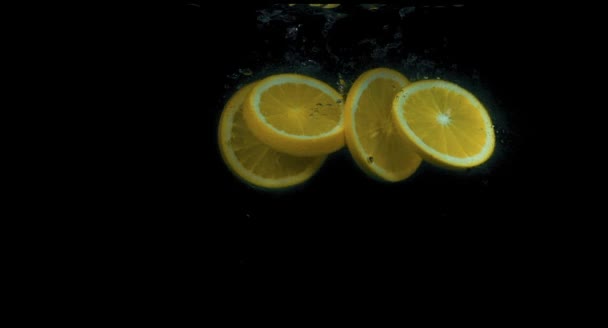 Апельсины падают в воду в замедленной съемке на черном фоне — стоковое видео