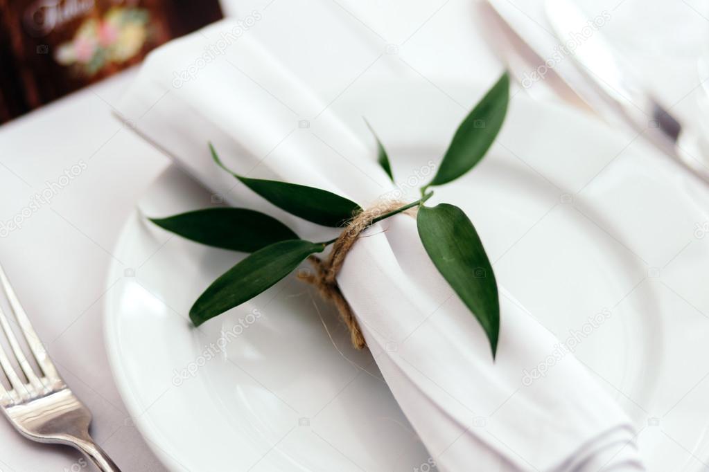 Napkin lying on a white dish tied up with twig.