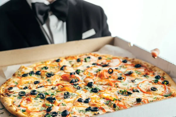 En man i kostym och fluga håller en låda pizza i sina händer.. — Stockfoto