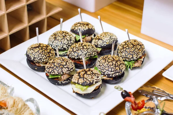 Un plato de mini hamburguesas, rollos negros espolvoreado con semillas de sésamo blanco. — Foto de Stock