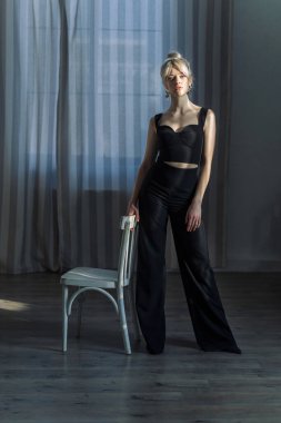 Siyah bluzlu ve siyah pantolonlu güzel bir sarışının stüdyo portresi yan tarafa bakıyor. Mavi gözler, genç ve narin 2.