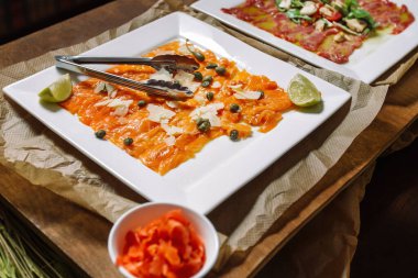 Somon carpaccio, kapari ve parmesan peyniri ile süslenmiş..