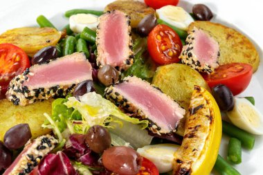 Beyaz tabakta servis edilen Nicoise salatası. Ton balıklı güzel salata, yumurta, domates ve patates..