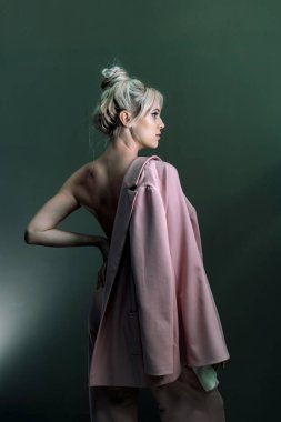 Elinde ceketle üstsüz duran seksi genç bir sarışın. Tam boy fotoğraf