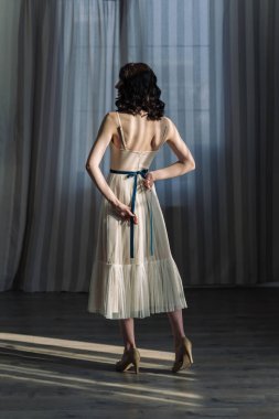 Stüdyoda perdelerin arkasında duran sevimli genç kız. Tam boy fotoğraf, ayaklı adımlar..