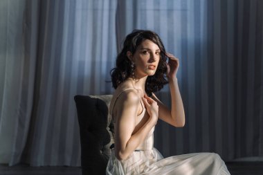 Güneşe bakan güzel bir esmerin stüdyo portresini kapat. Kahverengi gözlü, genç ve narin. Saçlarına elleriyle dokunuyor..