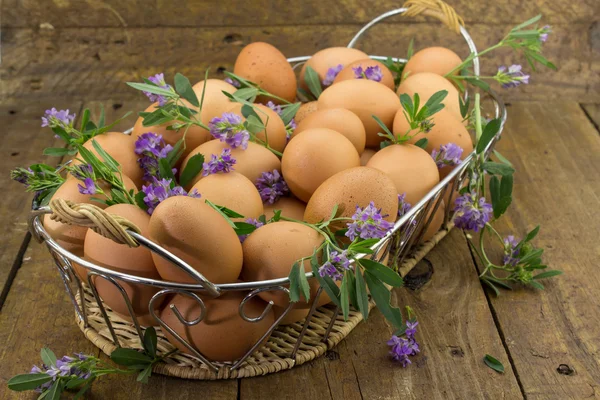 Зчеплення яєць і квітів в кошику на грубому дерев'яній лавці — стокове фото