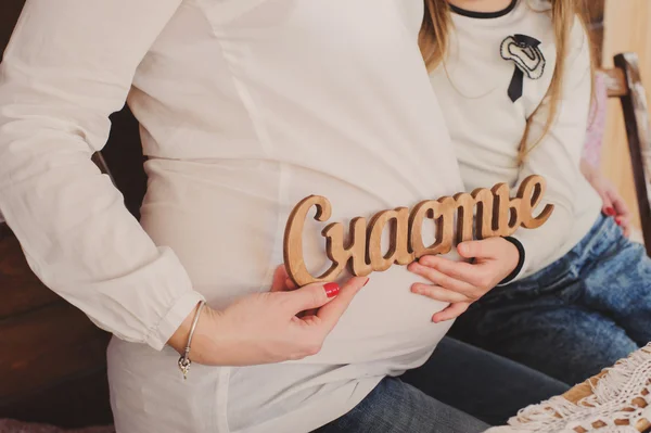 Mulher grávida abraça a barriga com a filha. Mãos segurar felicidade inscrição . — Fotografia de Stock