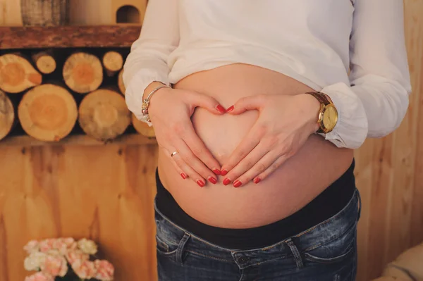 Mulher grávida abraça sua barriga. Mãos na forma de coração . — Fotografia de Stock