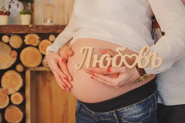Embarazada mujer abraza su vientre con husband.Hands mantener la inscripción amor . —  Fotos de Stock