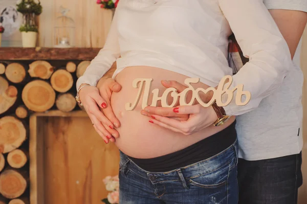 Mulher grávida abraça sua barriga com husband.Hands segurar amor inscrição . — Fotografia de Stock