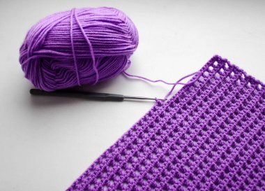 İplik yumağı, örgü kancası ve örülmüş keten parçası.