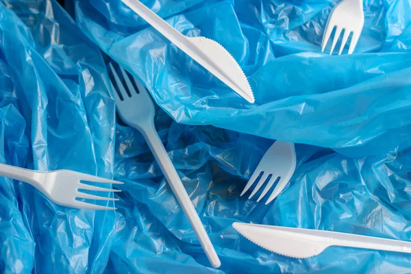 Plastic utensils, white forks and knives on a blue plastic bag. Abstract background. Environmental pollution, environmental problems