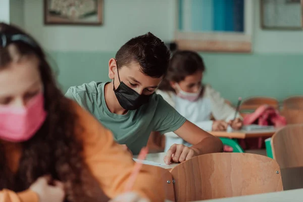 The boy is sitting at a school desk and wearing a mask on his face against corona virus protection. New normal. Education during the Covid-19 pandemic. Selective focus.High quality photo