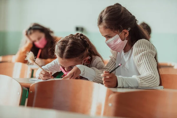 Little girls sitting at school desks while wearing a mask against pandemic corona virus protection. New normal. Education during the Covid-19 pandemic. Selective focus. . High quality photo