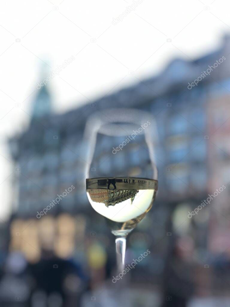 An inverted display of the historical building the Singer Book House in a glass of white wine in the historical center of St. Petersburg on the embankment of the Griboyedov Canal River in the summer of 2021