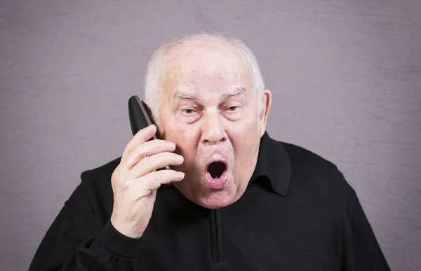 Hombre viejo muy emocional con el auricular del teléfono grita sobre un fondo gris —  Fotos de Stock