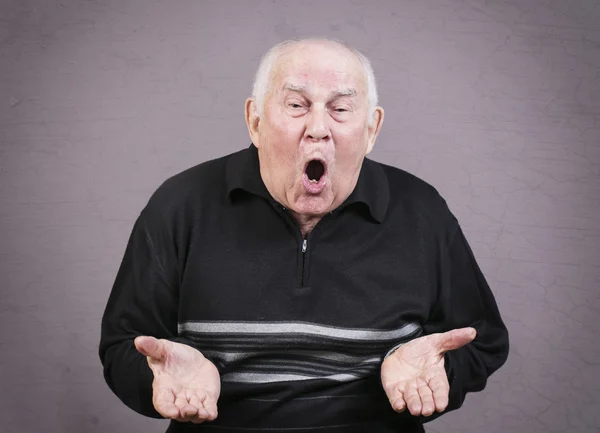 Un anciano muy emocional gesticula las manos sobre un fondo gris . —  Fotos de Stock