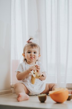 Sevimli küçük bebek kız mutfakta masada narenciye vitamin tam yiyor ve komik sevimli yüz yapıyor