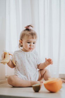 Sevimli küçük bebek kız mutfakta masada narenciye vitamin tam yiyor ve komik sevimli yüz yapıyor