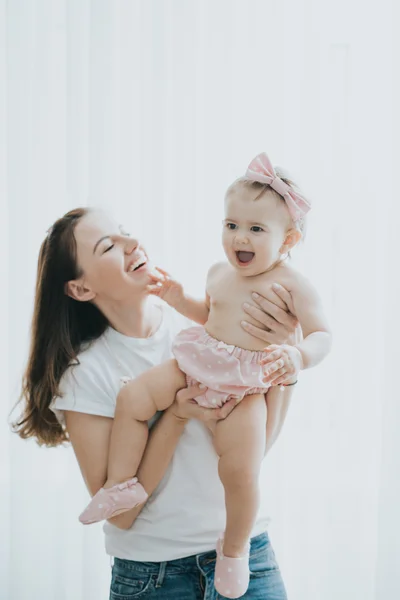 Beautiful mother portrait playing with her cute little girl in a white room in the morning — Stock Photo, Image