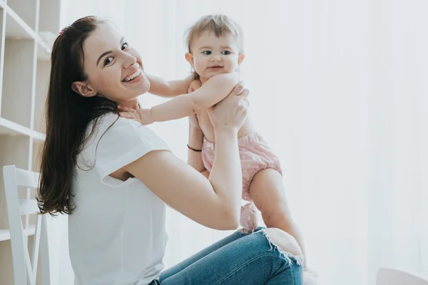 Beautiful mother portrait playing with her cute little girl in a white room in the morning — Stock Photo, Image