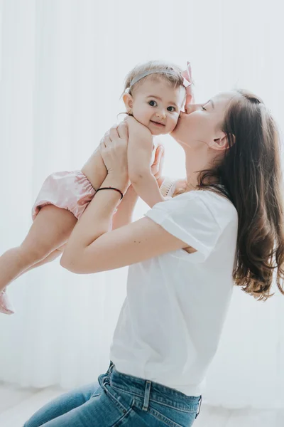 Beautiful mother portrait playing with her cute little girl in a white room in the morning — Stock Photo, Image