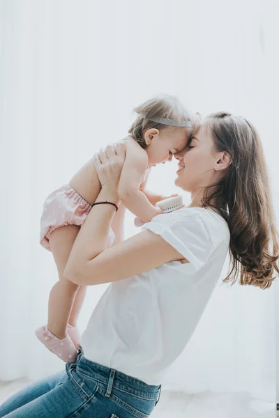 Beautiful mother portrait playing with her cute little girl in a white room in the morning — Stock Photo, Image