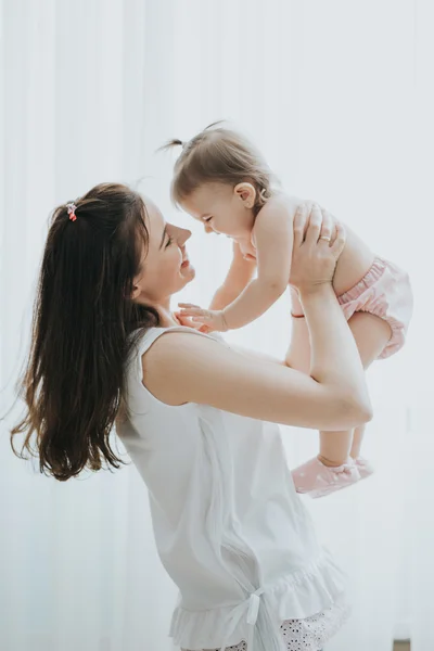 Bela mãe retrato brincando com sua menina bonito em um quarto branco na parte da manhã — Fotografia de Stock