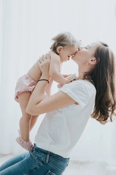 Beautiful mother portrait playing with her cute little girl in a white room in the morning — Stock Photo, Image