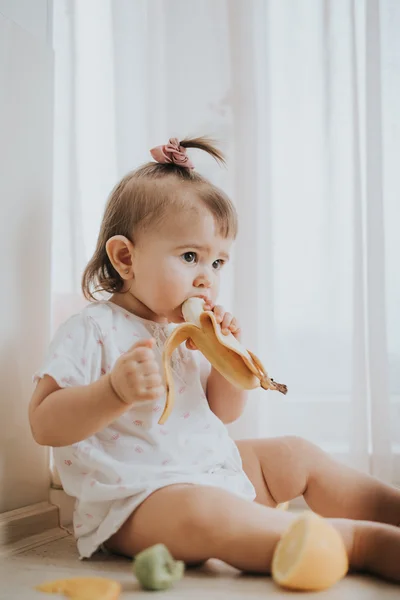 Cute little baby girl on the table in the kitchen eats citrus fruits full of vitamins and makes funny cute faces — Stock Photo, Image