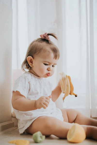 Милая маленькая девочка на столе на кухне ест цитрусовые, полные витаминов и делает смешные милые лица — стоковое фото