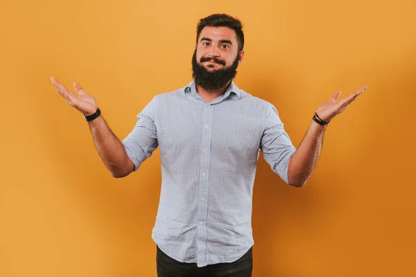 Portret van knappe lachende man geïsoleerd op gele studio achtergrond poseren voor de camera en het maken van grappige gezichten, vergelijken met handen — Stockfoto