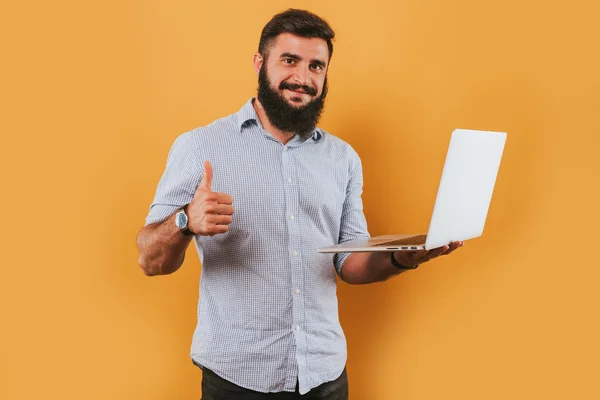 Portret van knappe lachende man geïsoleerd op gele studio achtergrond poseren voor de camera en het maken van grappige gezichten, kreeg idee, wijzend op de monitor werkende laptop computer — Stockfoto