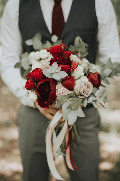 Porträt eines Bräutigams, der mit einem Blumenstrauß in der Hand im Wald bei Sonnenuntergang posiert — Stockfoto