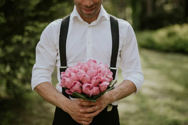 夕日の森で彼の手の花の花束とポーズの結婚式新郎の肖像画 — ストック写真