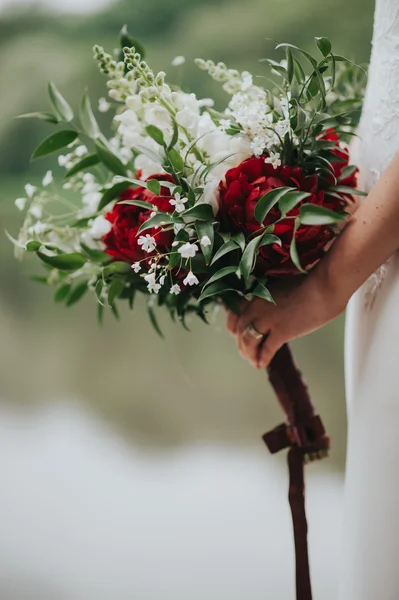 Porträt einer Hochzeitsbraut, die in einem weißen Hipster-Kleid mit Blumen in den Händen im Wald bei Sonnenuntergang posiert — Stockfoto