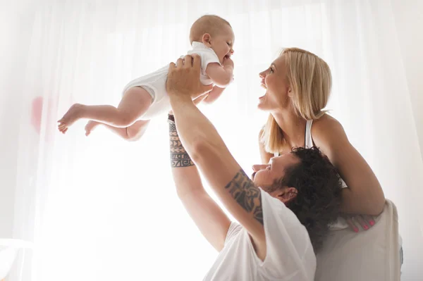 Casal sorridente brincando com seu bebê recém-nascido amado no sofá — Fotografia de Stock