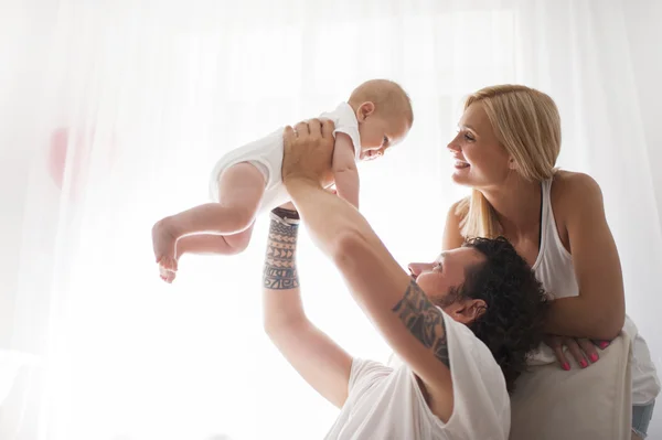 Casal sorridente brincando com seu bebê recém-nascido amado no sofá — Fotografia de Stock