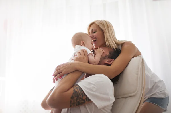 Casal sorridente brincando com seu bebê recém-nascido amado no sofá — Fotografia de Stock
