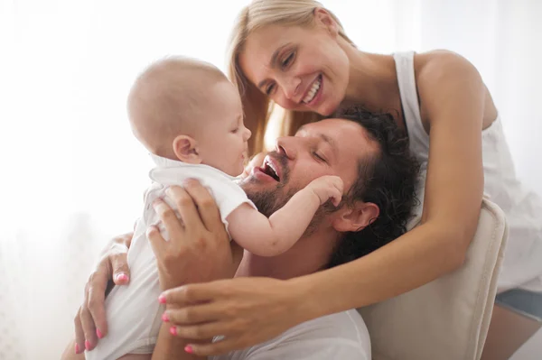 Casal sorridente brincando com seu bebê recém-nascido amado no sofá — Fotografia de Stock