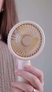 Açık havada güneşli bir günde mini yelpazesinden serin havanın tadını çıkaran genç bir kadın. Yüksek kalite 4k görüntü